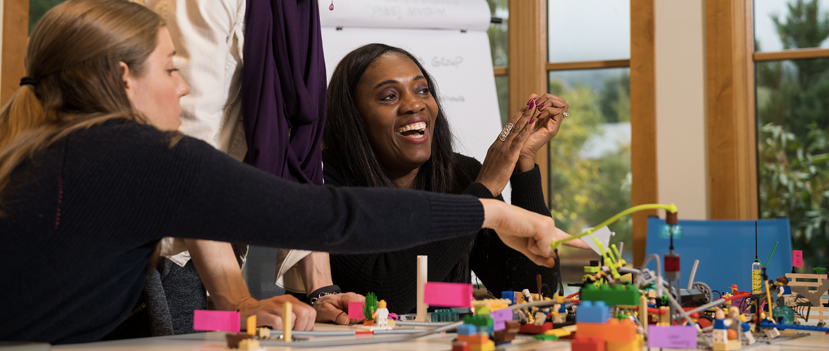 Two women laugh and discuss their creation at a LEGO Team Building event